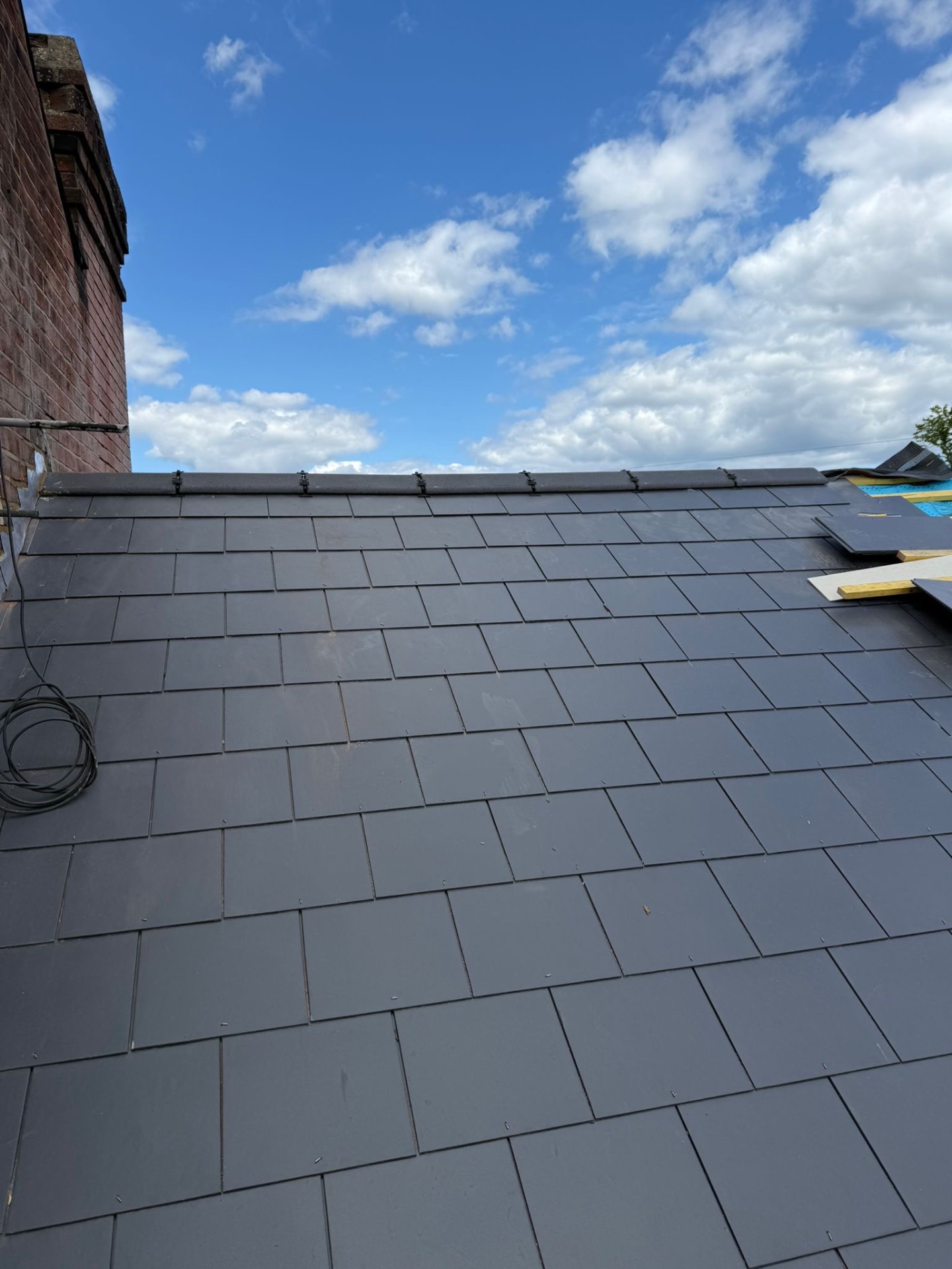 Sweeping view of a freshly laid grey slate roof under bright blue sky