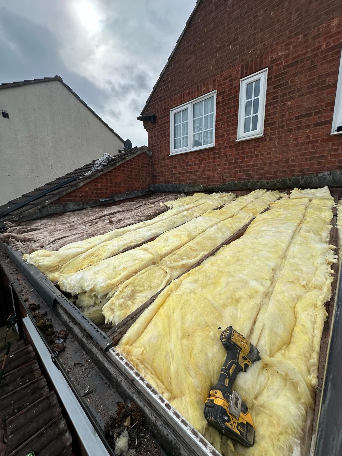 Flat roof insulation upgrade with yellow mineral wool laid between joists