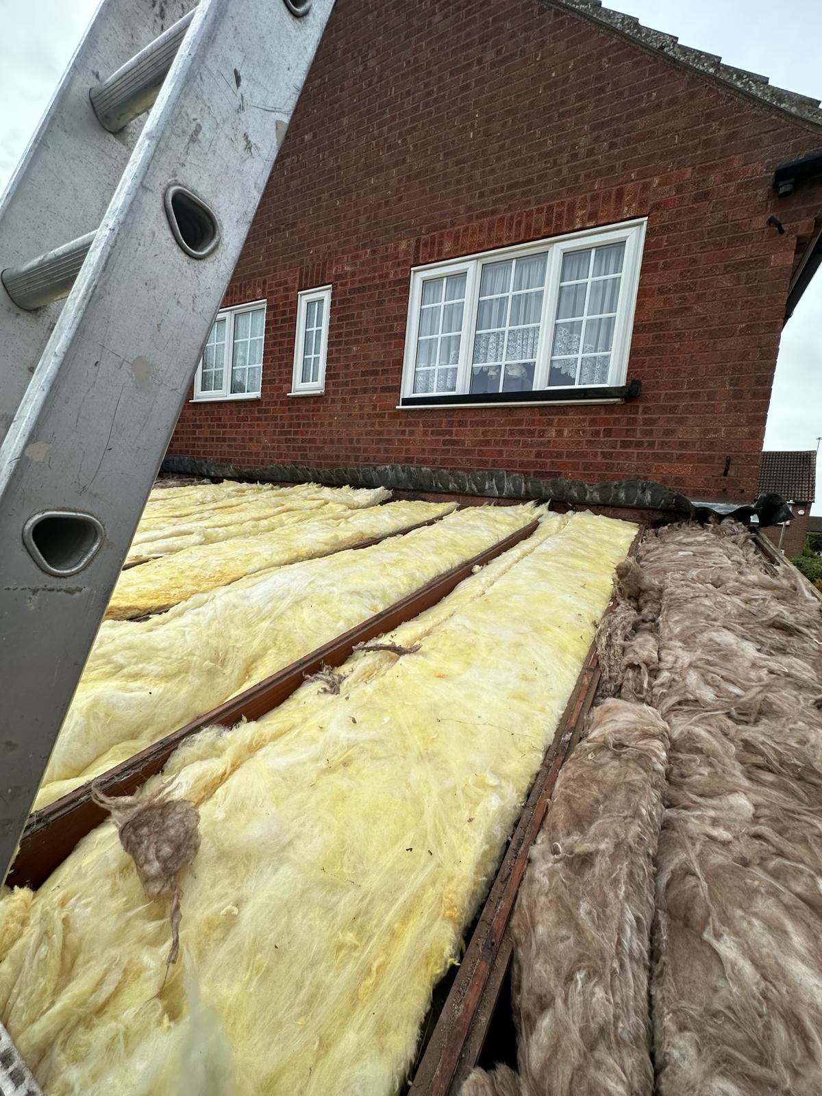 Roof stripped back exposing yellow mineral wool loft insulation between rafters