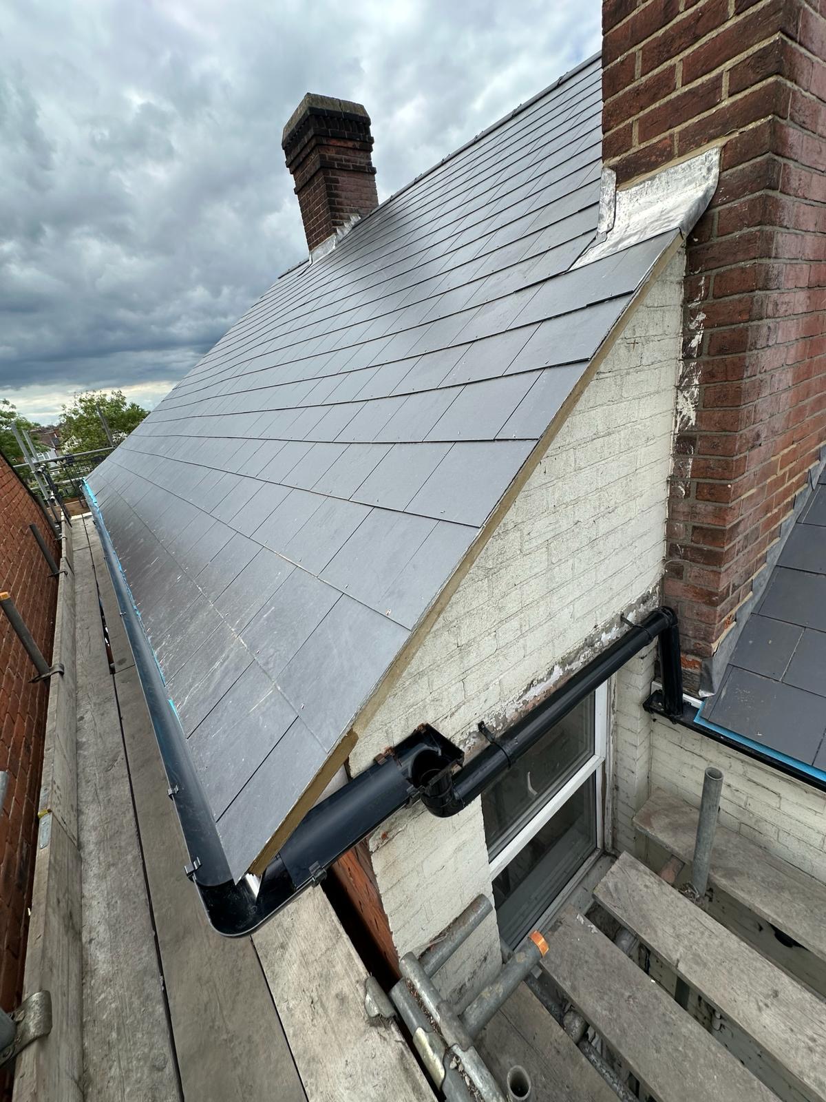 Slated dormer cheek dressed with lead against a painted brick wall