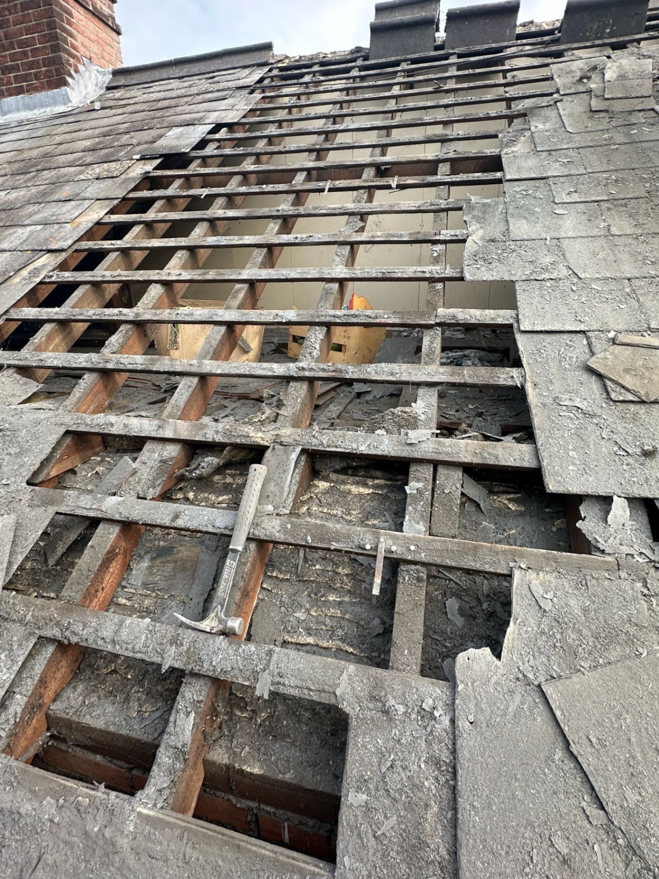 Roof strip in progress with hammer and stripped slates on battens