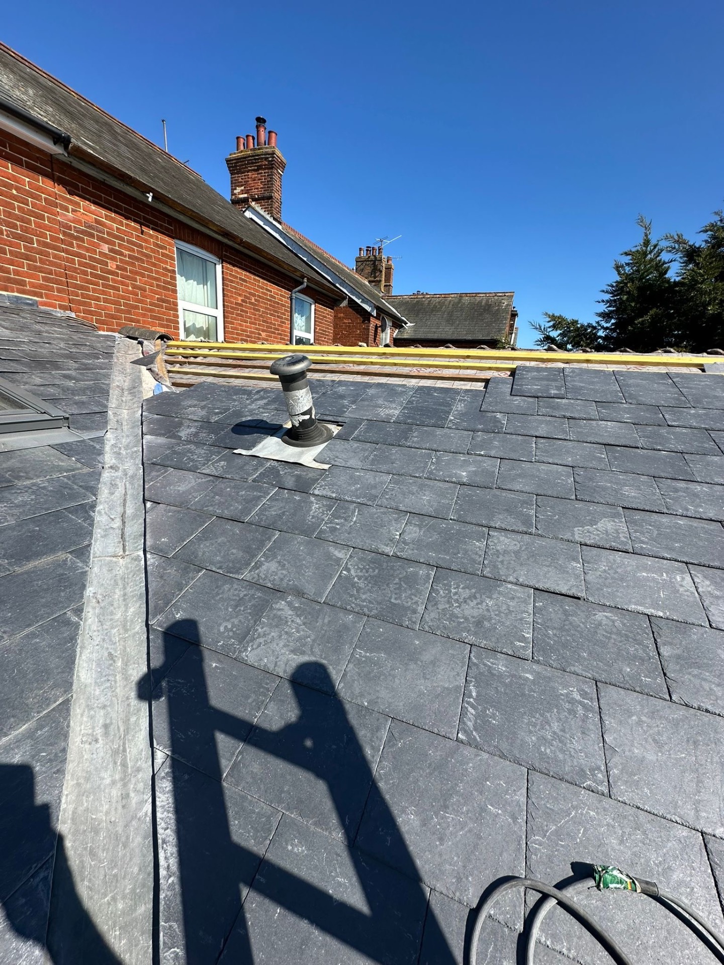 Completed grey slate pitched roof with brick chimney stacks under blue sky