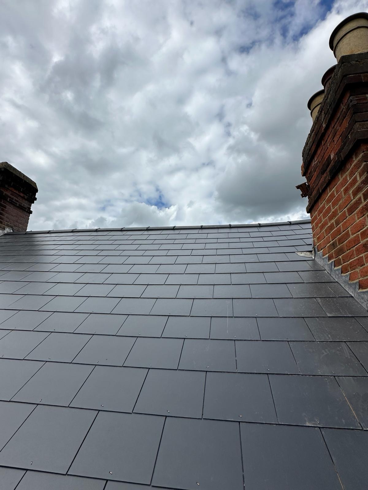 Uplooking view of neat slate courses running toward a red brick chimney