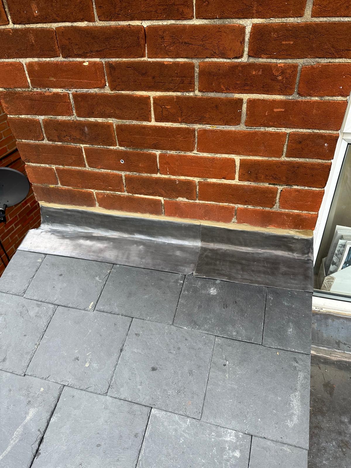 Neat lead flashing along brick wall on newly laid slate roof
