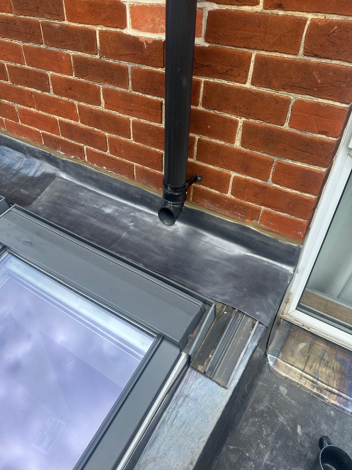 Lead flashing around downpipe on flat roof next to skylight