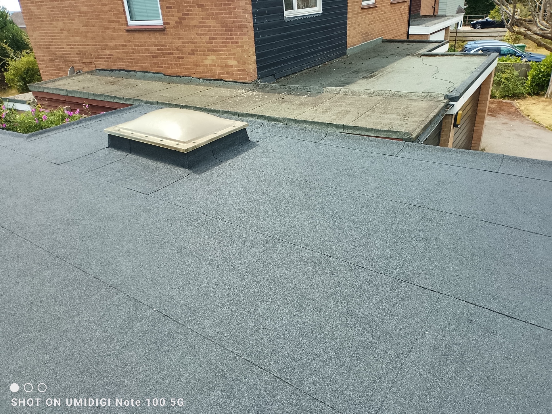 Freshly finished torch-on felt flat roof with skylight dome on garage extension