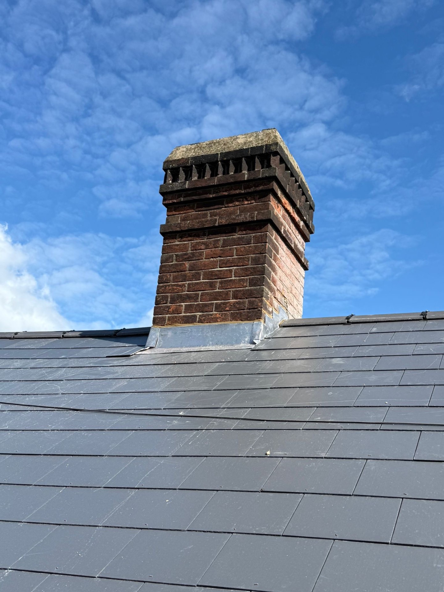 Freshly re-leaded chimney stack rising above new grey slate roof