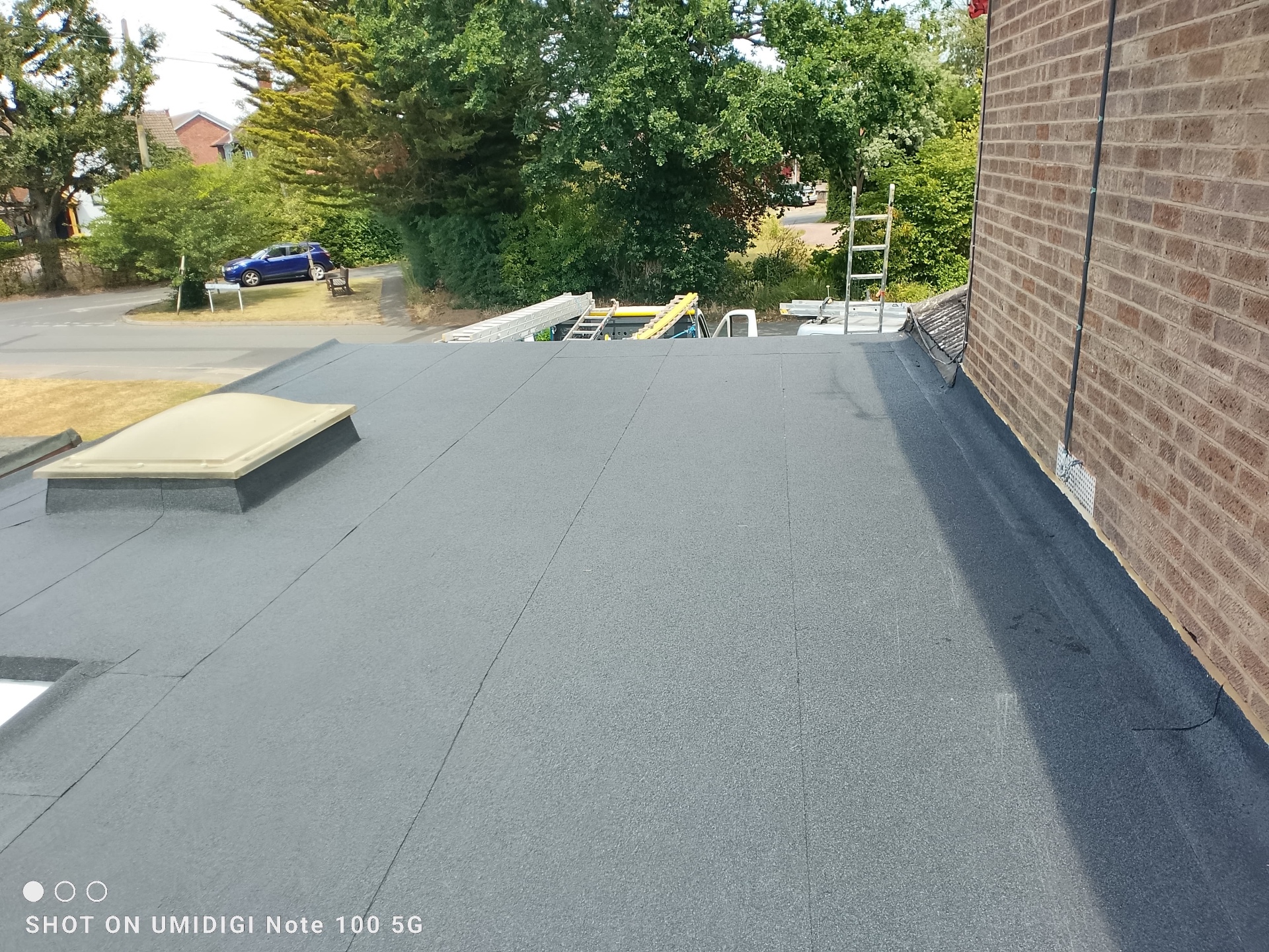 Smooth new torch-on felt flat roof with skylight and crisp edge detail against brickwork