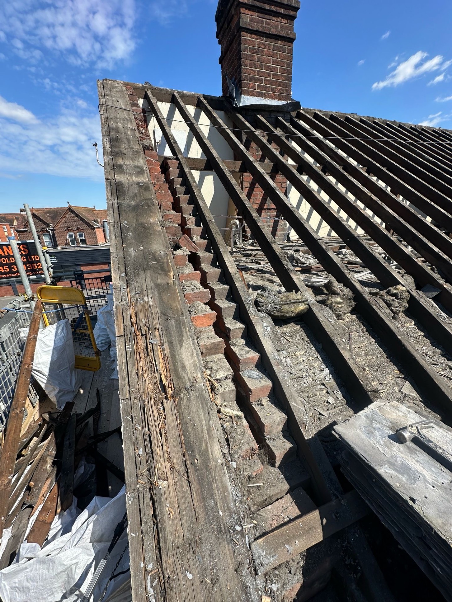 Bare roof rafters between chimney stacks under bright blue sky
