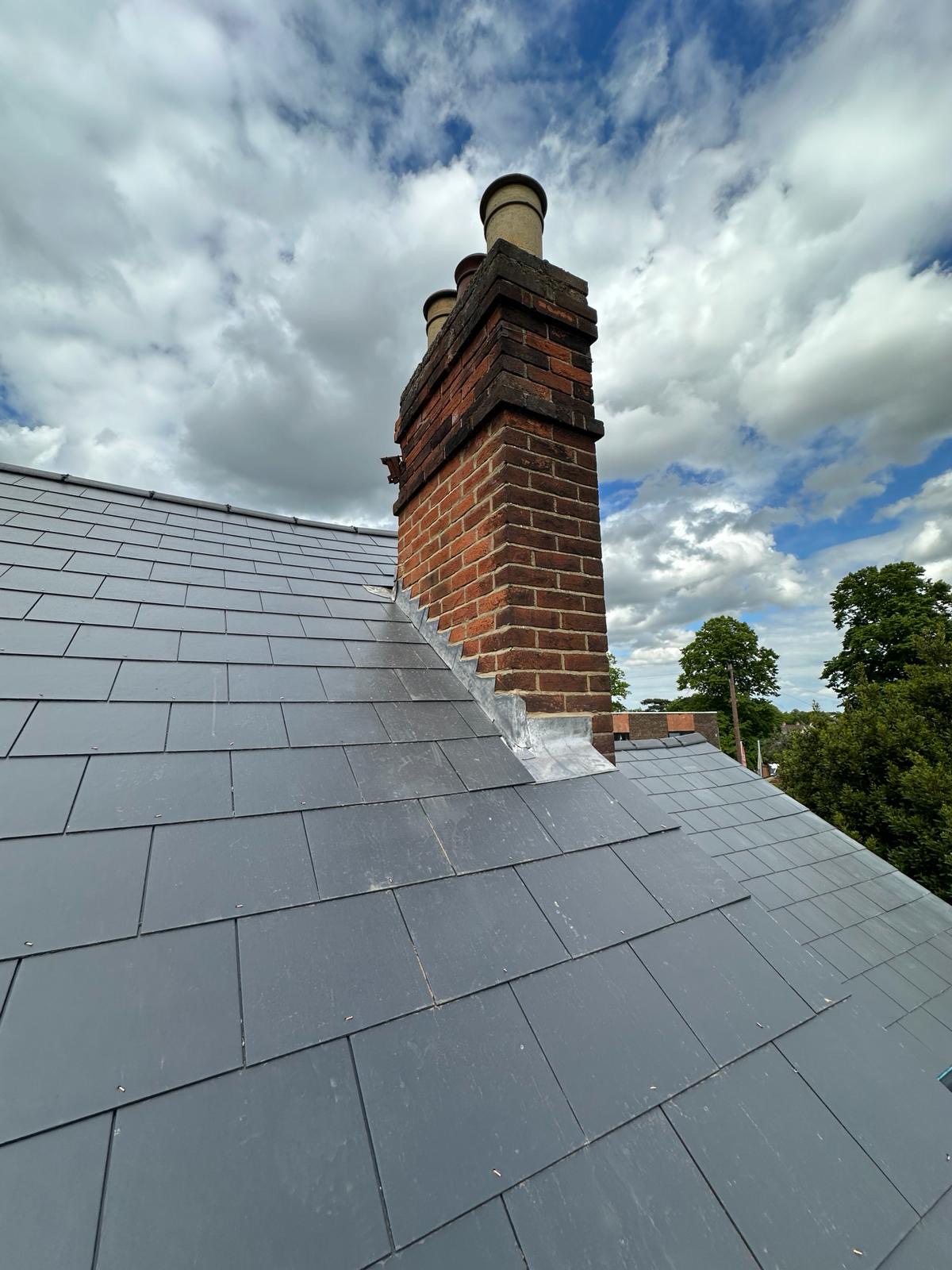 New slate roof meeting stepped lead flashing at a red brick chimney stack