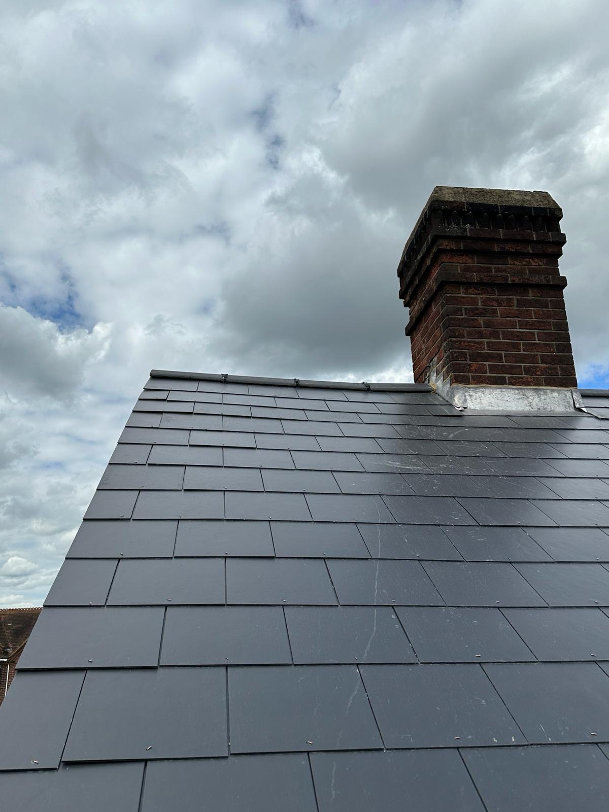 Fresh grey slate roof meeting old red brick chimney under cloudy sky