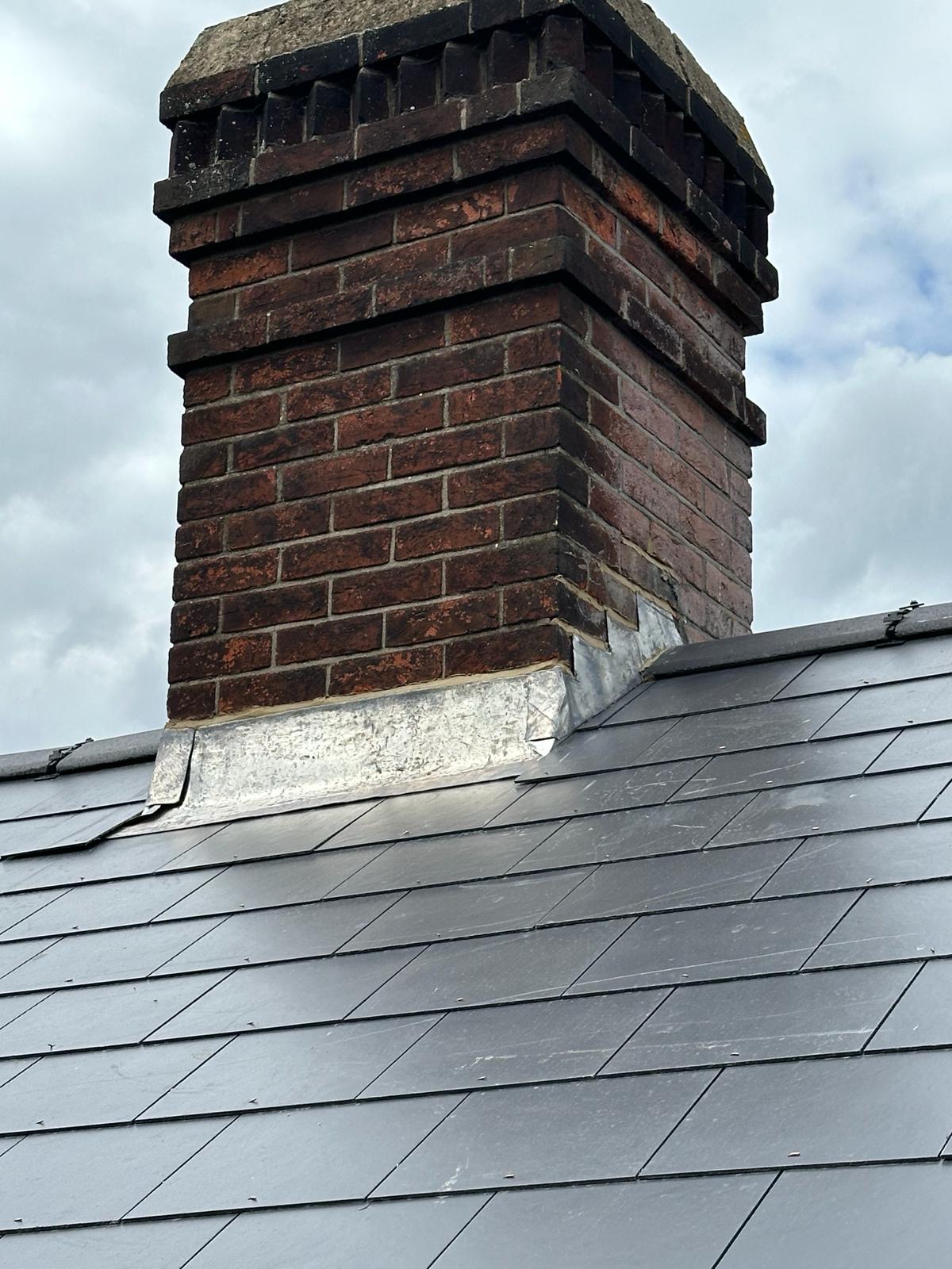 Close-up of weathered brick chimney with fresh lead flashing on slate roof