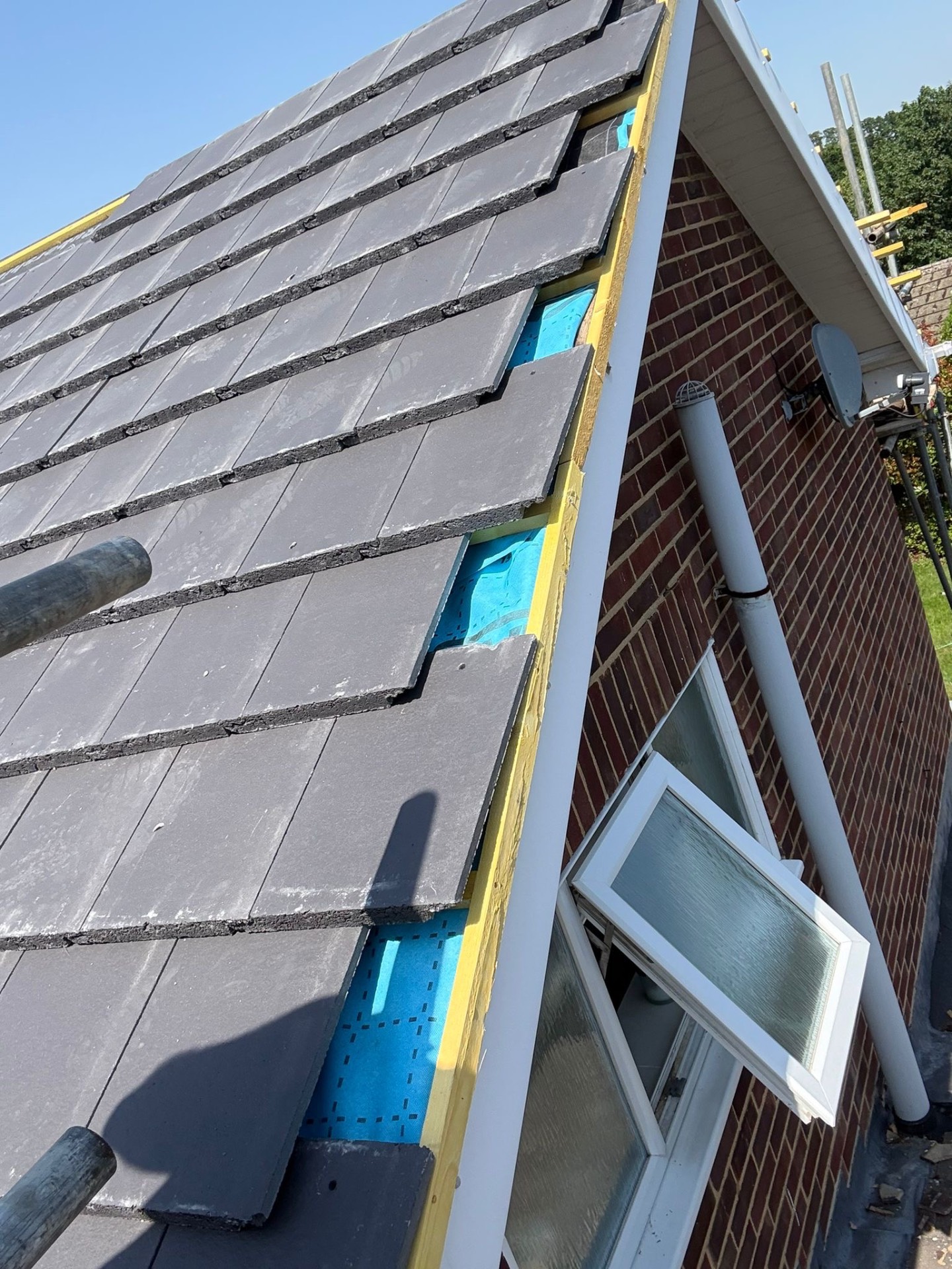 Close-up of new grey slate tiles being laid over blue Wraptor membrane on a gable