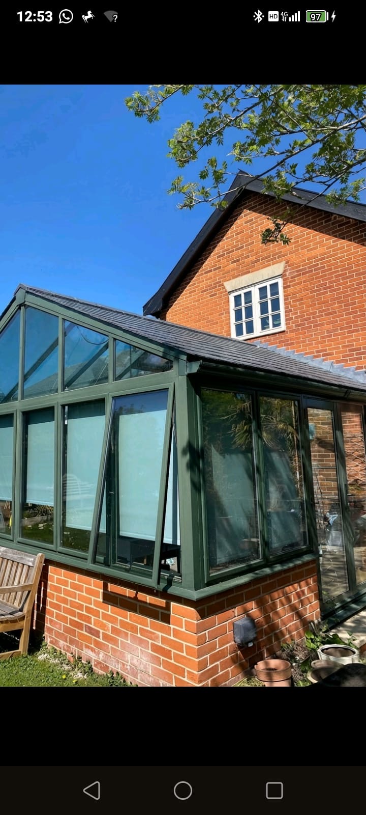Green-framed pitched conservatory roof with fresh grey tiles against red brick house