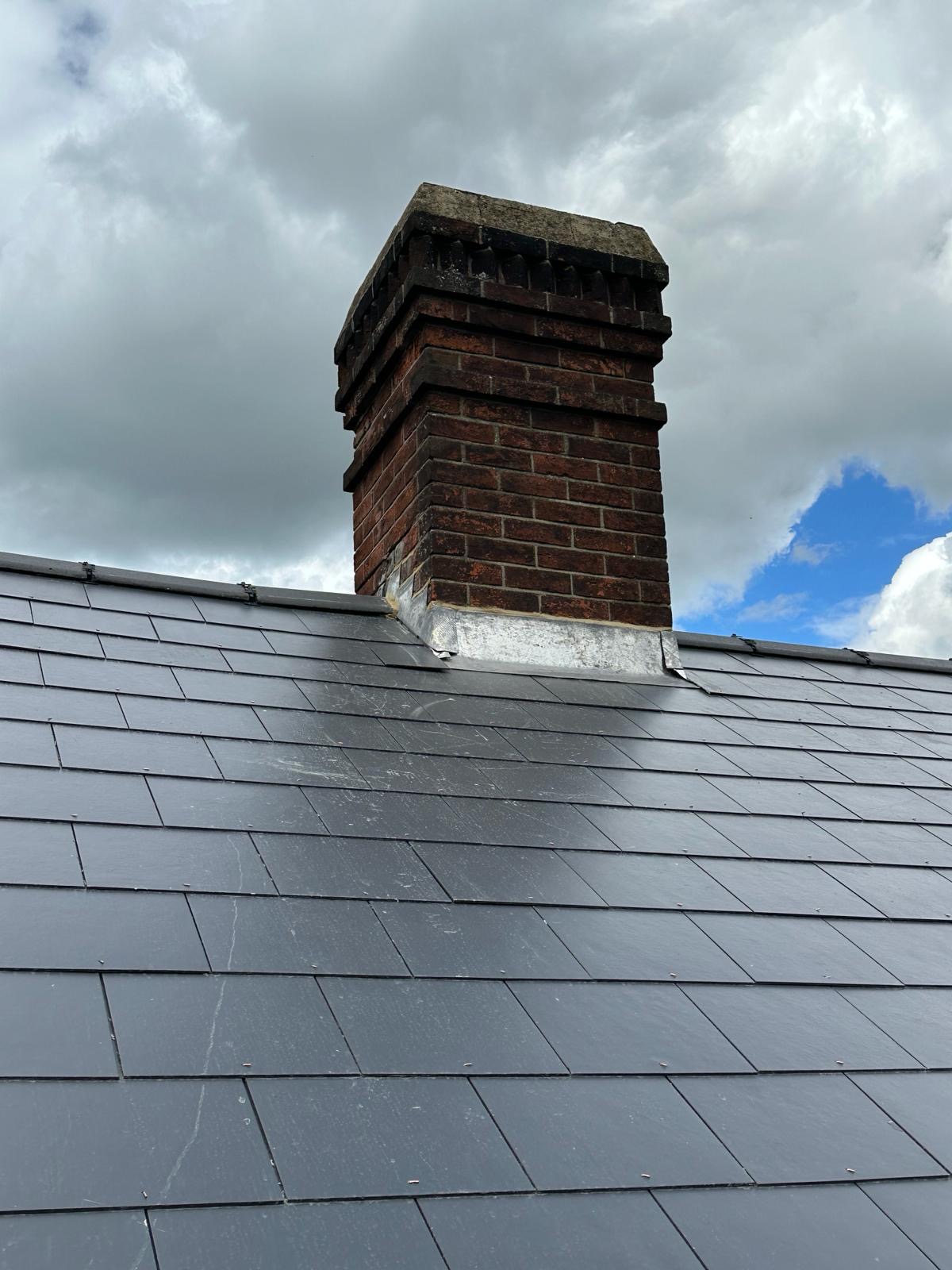 Ornate red brick chimney rising above new slate roof with lead apron