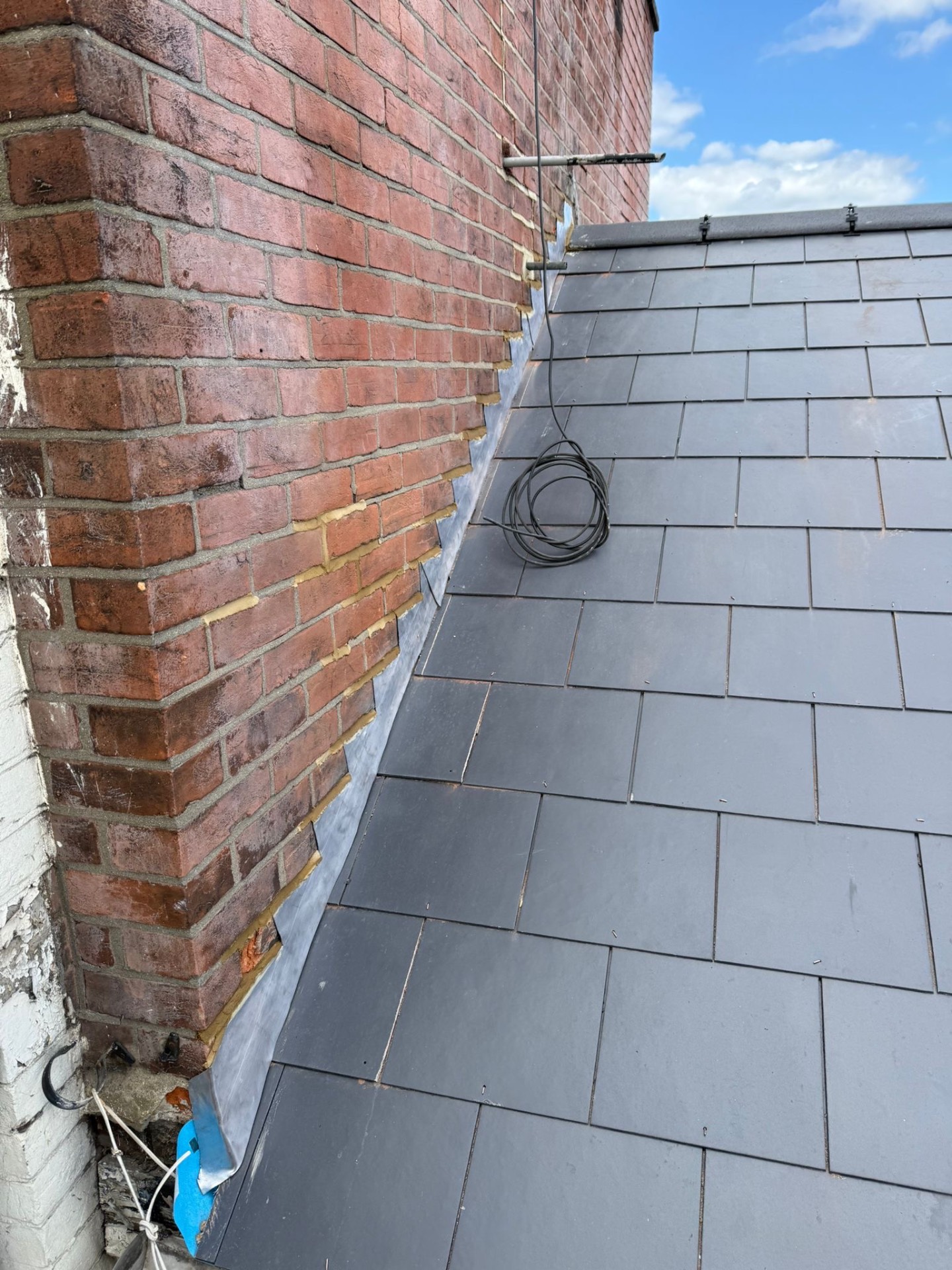 Precision lead flashing tucked neatly between slate roof and old red brickwork