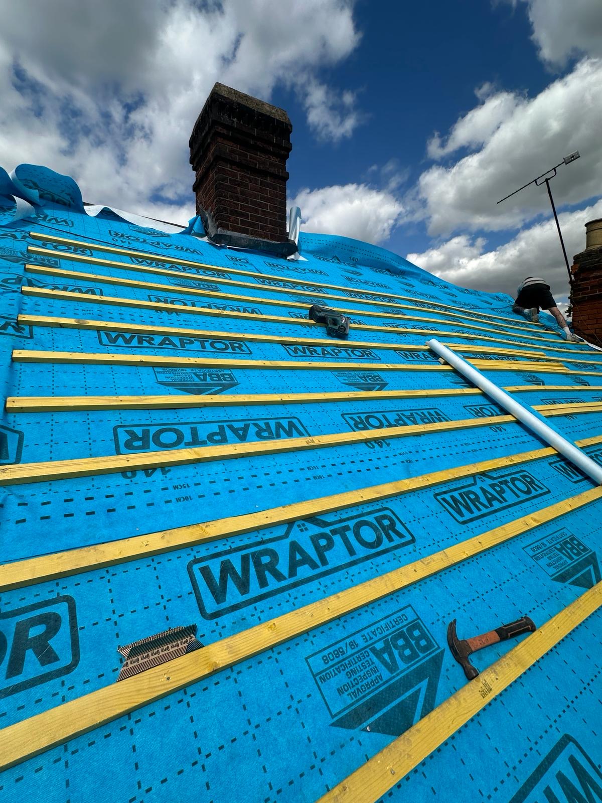 Roofer nailing battens over Wraptor membrane beside chimney stack